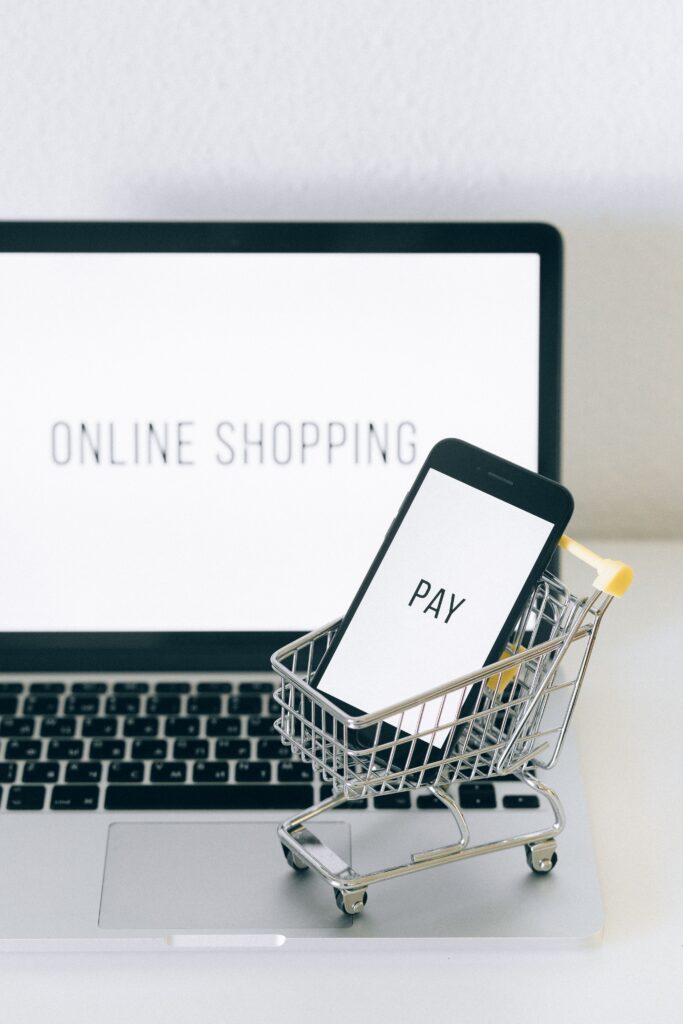 A smartphone in a miniature cart on a laptop symbolizes online shopping and digital payment.